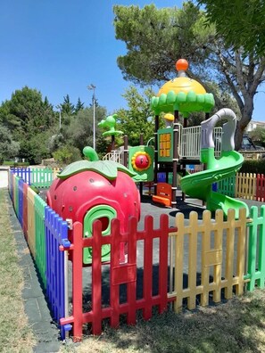 Ein Spielbereich für Kinder mit einer großen roten und grünen Konstruktion, einer gelben Kuppel und einer Rutsche.