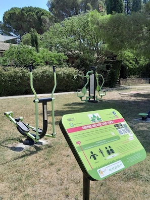 Draußen aufgestellte Fitnessgeräte und ein Schild mit Informationen.