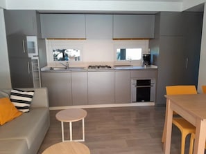 Eine kompakte Küche mit grauen Schränken, einem eingebauten Backofen und einem Essbereich mit Holztisch und Stühlen.