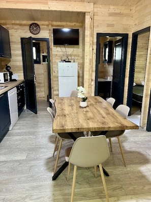 Ein Holzinterieur mit einem Esstisch, Stühlen, einer Uhr, einem Fernseher und einem Kühlschrank.