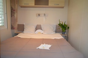 A bedroom with a bed, two bedside tables, a potted plant, and a window with curtains. - Camping 3 étoiles - Piscine  - ccbg0d0 (Molières)