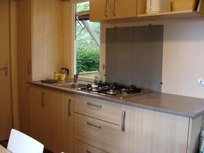A compact kitchen with wooden cabinets, a gas stove, and a window with a view of greenery. - Camping 3 étoiles - Piscine  - ccbg0d0 (Molières)