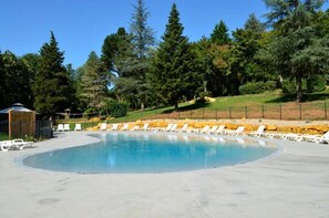 Ein Swimmingpool mit Liegestühlen, umgeben von Bäumen und einer Rasenfläche.