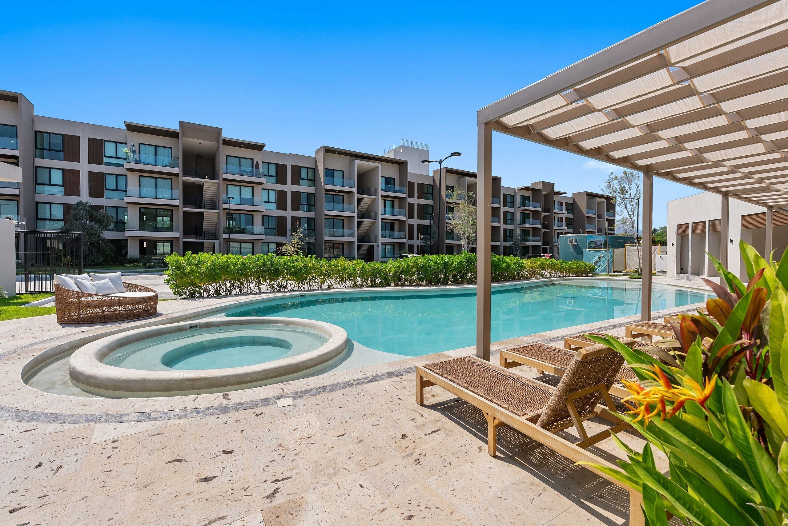 A swimming pool with lounge chairs and a hot tub, surrounded by a building with balconies.