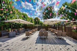 Eine Terrasse im Freien mit Holzboden, mehreren Tischen und Stühlen sowie bunten, dreieckigen Wimpeln.