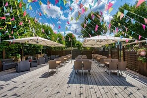 Eine Terrasse im Freien mit Holzboden, mehreren Tischen und Stühlen sowie farbenfrohen dreieckigen Flaggen.