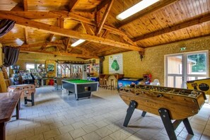 Un espace de loisirs intérieur doté d’un plancher en bois, comprenant une table de billard, un baby-foot et divers jeux électroniques.
