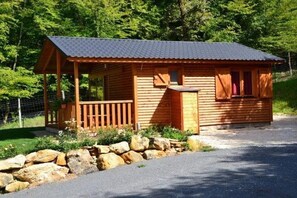 Une cabane en bois avec un porche, un petit abri attenant et un mur de pierres à l’avant.