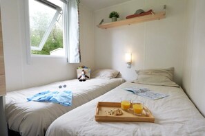 A room with two beds, a window with curtains, a shelf with items, and a tray with cookies and juice. - Camping 3 étoiles - Piscine  - ccaf0di (Vensac)