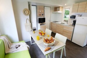 A modern kitchen with a dining area, a sofa, and breakfast items on the table. - Camping 3 étoiles - Piscine  - ccaf0di (Vensac)