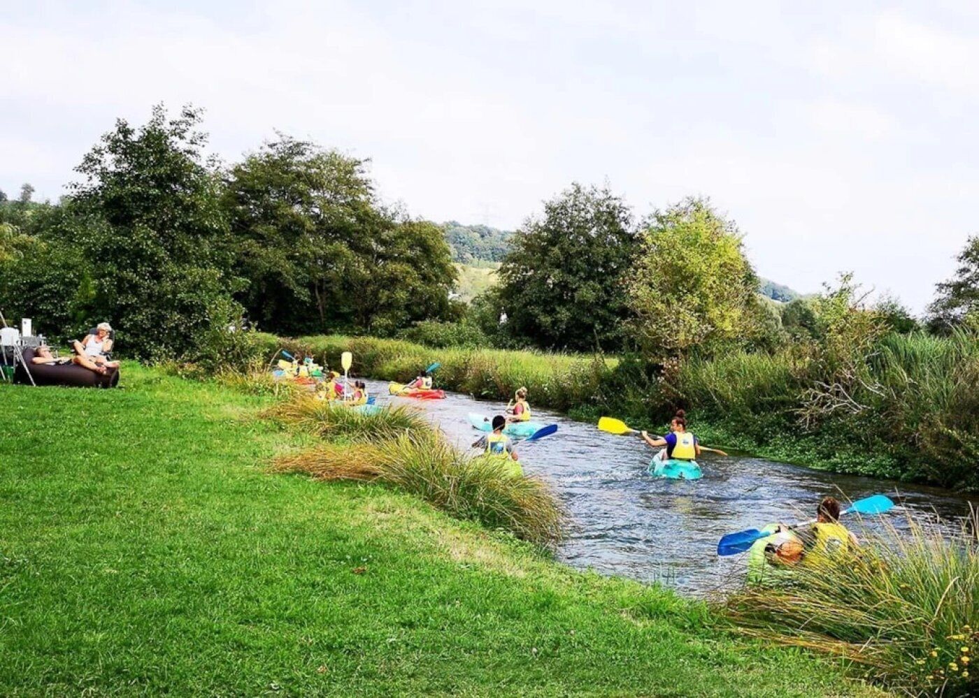 En gruppe mennesker roer i kajak på en flod omgivet af grøn vegetation.