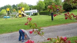 Un camí pavimentat amb un nen agenollat, un parc infantil amb elements grocs, i gespa verda al fons.