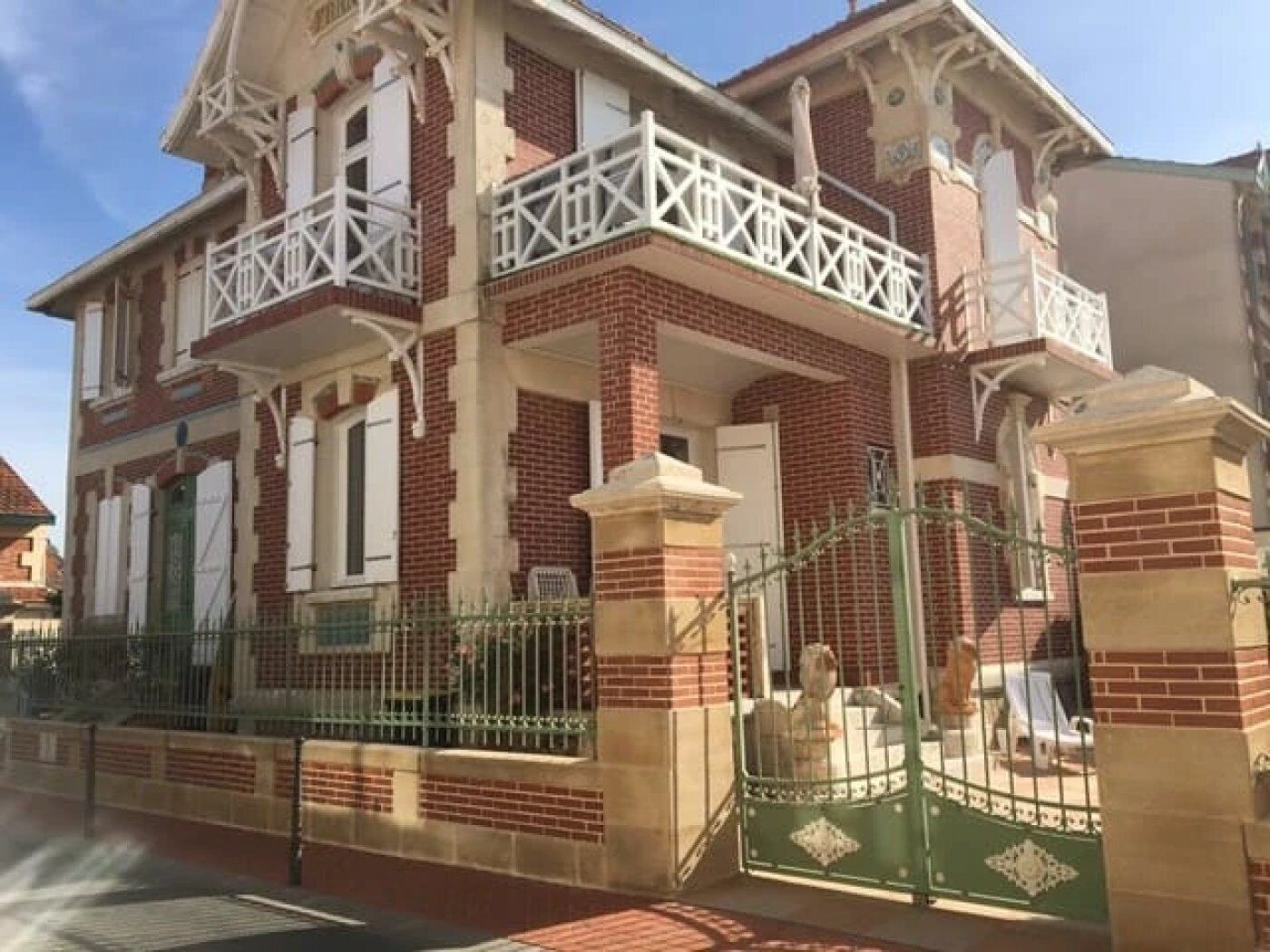 Un edificio de dos pisos con fachada de ladrillo, balcones blancos y una entrada con portón.