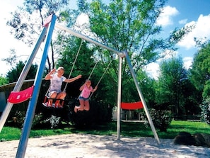 Eine Schaukel im Park mit Bäumen und blauem Himmel.