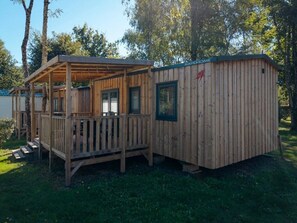 Eine Holzhütte mit Veranda und einem separaten Gebäude, vermutlich ein Badehaus, in der Nähe eines Gewässers.