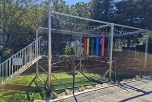 Ein Spielplatz mit einer Kletterkonstruktion, einem Netzbereich und einer Rasenfläche.