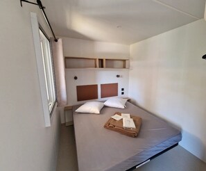 Ein Einzelbett mit Kopfteil, einem Fenster und einem Wandregal.