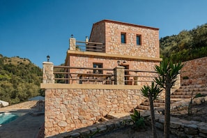 Ein Steinhaus mit Pool, Sitzgelegenheiten im Freien und einer Treppe, die zu einem Balkon führt.