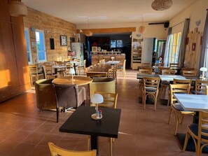A restaurant with multiple dining tables and chairs, wooden walls, and a kitchen area in the background.