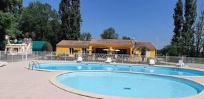 A swimming pool with a fenced area, a yellow building with a tiled roof, and trees in the background.