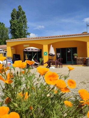 Un edificio amarillo con mesas al aire libre, un letrero de salida verde y un cielo despejado.
