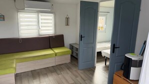 Une pièce de taille modeste, comprenant un canapé, un lit, une porte et une petite table avec une poubelle.