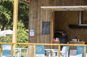 En madvogn med et krittavle-menu der viser retter som crepes og gratin. Udendørs siddepladser og en person står bag disken.