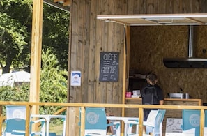 En madvogn med et krittavle-menu der viser retter som crepes og gratin. Udendørs siddepladser og en person står bag disken.
