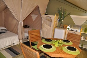 Ein Zeltraum mit einem Bett, einer kleinen Küchenzeile, einem Esstisch mit grünen Platzsets und einem Stuhl.