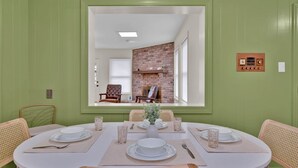Uma sala de jantar com lareira de tijolos, paredes verdes e um espelho grande que reflete o ambiente.