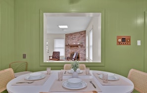 A dining room with a brick fireplace, green walls, and a large mirror reflecting the room. - Retro Time Capsule · Mid-Century 3BR · Sleeps 9 (Shreveport)