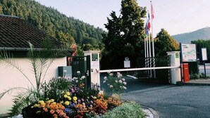 A gated entrance with a flower bed, a flag, and a signboard.