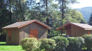 Two small wooden cabins with pitched roofs, surrounded by dense greenery and trees.