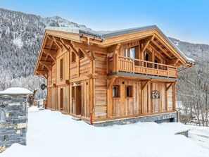 Eine Holzhütte mit Balkon, Steinunterbau und einem Bergpanorama.