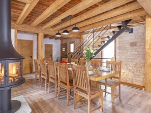 Ein Essbereich mit Kamin, Holzstühlen, einem Tisch für vier Personen und einer Treppe, die in eine obere Ebene führt.