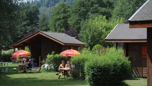 A rustic outdoor area with wooden cabins, picnic tables, and umbrellas.
