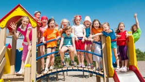 Children playing on a playground with a slide and climbing structure.