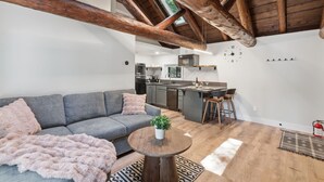 Ein modernes Interieur mit einer Loft-Decke, einem grauen Sofa, einem kleinen runden Tisch mit einer Pflanze und einer Küchenzeile im Hintergrund.