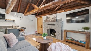 Ein modernes Wohnzimmer mit Kamin aus Stein, Holzbalken, einer Couch und einem Essbereich.
