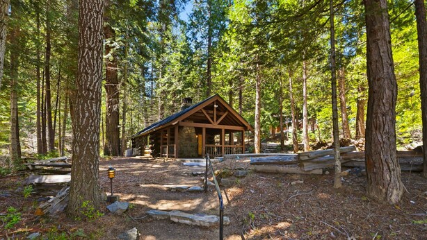 Eine Lodge mit Steinfundament, Holzständern und einem Satteldach, umgeben von einem Wald.
