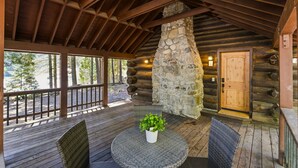 Eine Blockhütte mit Kamin aus Stein, einer Holzterrasse und einem runden Tisch mit Stühlen.