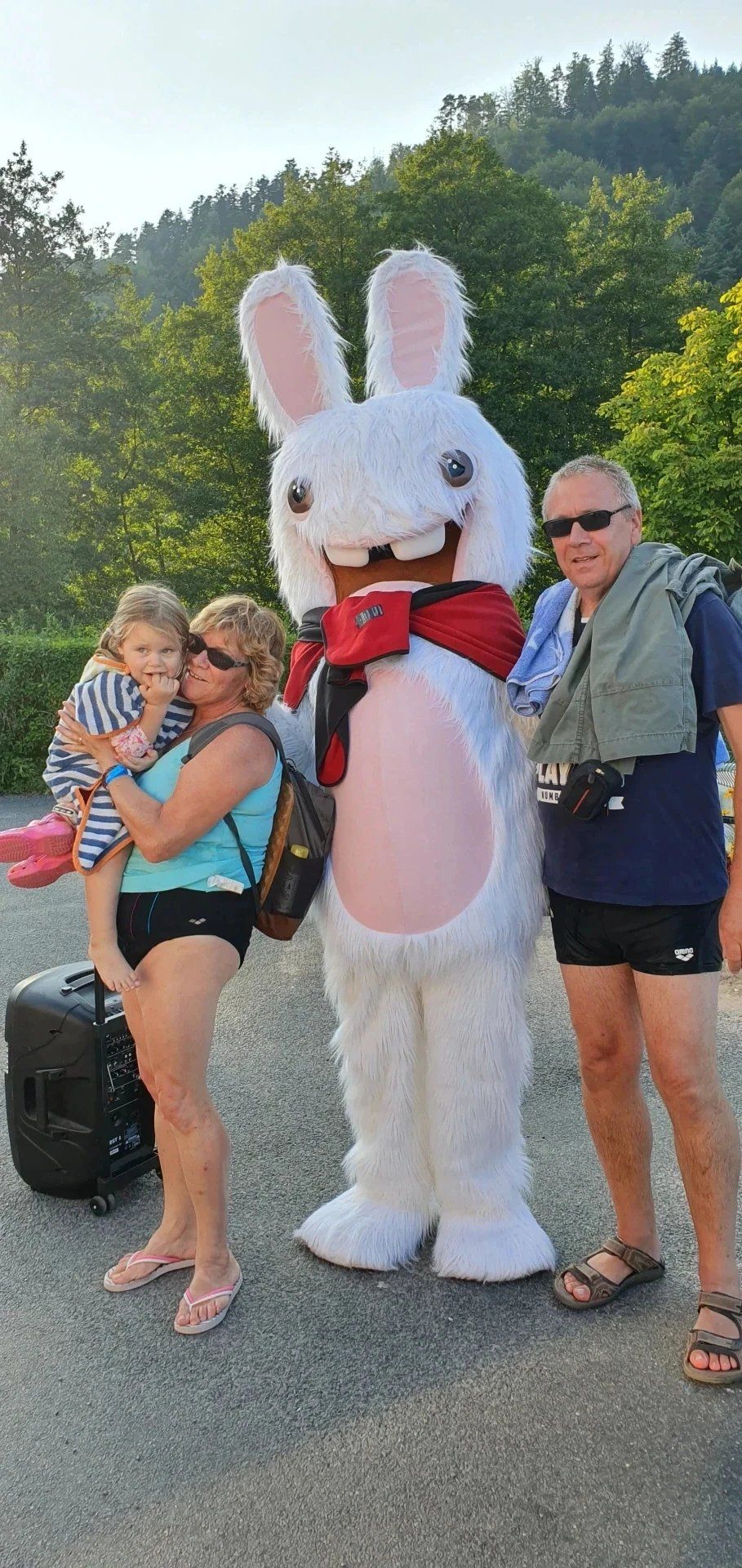 A person in a white rabbit costume standing outdoors with a child and an adult.