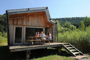 Eine Holzhütte mit einer Terrasse, großen Fenstern und einer Leiter, die zum Eingang führt.