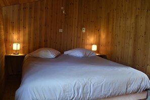 Ein Zimmer mit Holzwänden, einem Bett, zwei Nachttischlampen und einem Thermostat an der Wand.