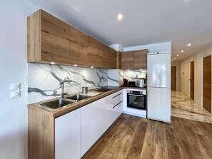 A modern kitchen with wooden cabinets, a marble backsplash, and a built-in oven. - 2nd floor, terrace, tv, 75m², Serre Chevalier (Briançon)