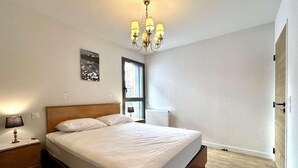 Un dormitorio con cama, mesita de noche, lámpara, candelabro, ventana y radiador.