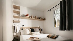 Une chambre à coucher comprenant un lit, des tables de chevet, une fenêtre avec des rideaux et des étagères intégrées.