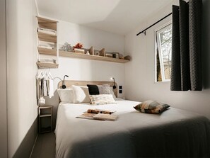 Ein Schlafzimmer mit einem Bett, Nachttischen, einem Fenster mit Vorhängen und eingebauten Regalen.