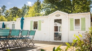 A row of white mobile homes with green shutters, a table with chairs, and a wooden deck. - Camping 4 étoiles - ccbg0id (Saint-Éloy-les-Mines)