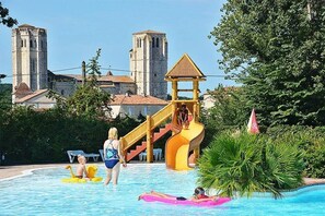 A swimming pool with a water slide, a castle-like building in the background, and lush greenery. - Camping 4 étoiles - Parc aquatique - ccbfhdg (La Romieu)